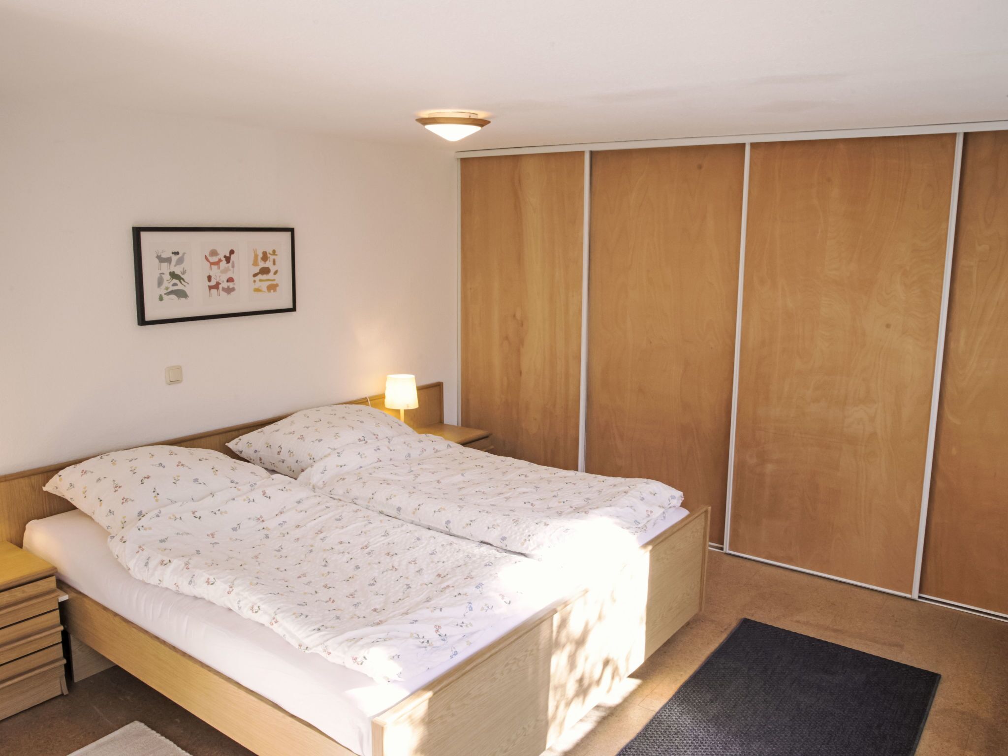 Una camera da letto con un letto, comodini, una lampada da parete, un quadro incorniciato e un armadio in legno.