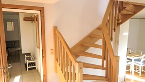 Eine Holztreppe führt zu einer zweiten Etage, einem Essbereich mit weißen Stühlen und einer Tür, die in einen anderen Raum führt.