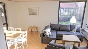 Ein modernes Wohnzimmer mit einer Couch, Sesseln, einem Esstisch und einem großen Fenster.