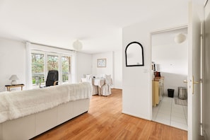 Ein moderner, gut beleuchteter Raum mit einem großen Fenster, einem Essbereich und einer durch eine offene Tür einsehbaren Küche.