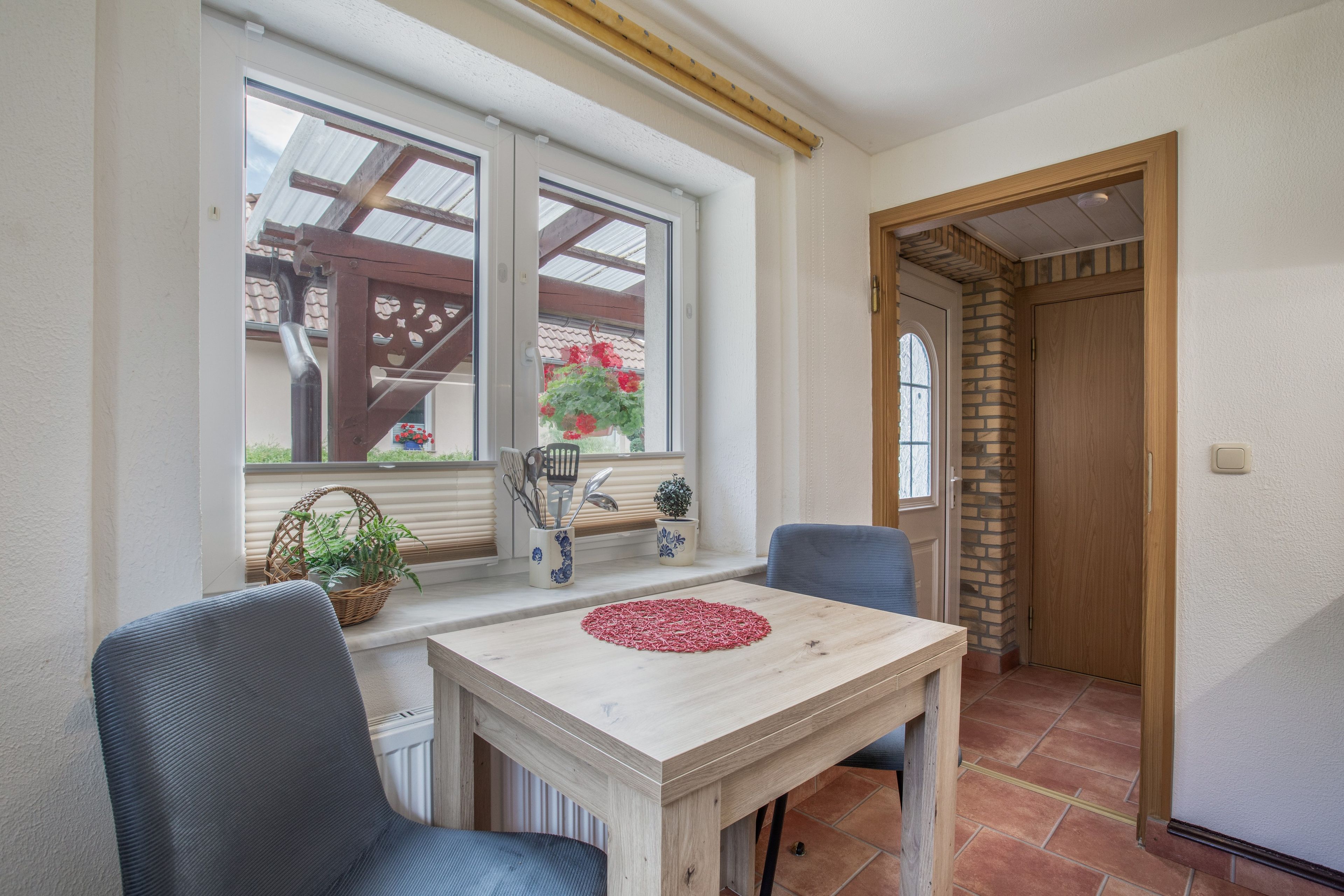 Ein Essbereich mit Tisch und Stühlen, ein Fenster mit Aussicht und eine Tür zu einem weiteren Raum.