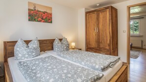 A bedroom with a wooden wardrobe, a bed with floral bedding, and a painting of flowers on the wall. - Apartment “Max” with Private Terrace, Garden, and Wi-Fi (Heringsdorf)