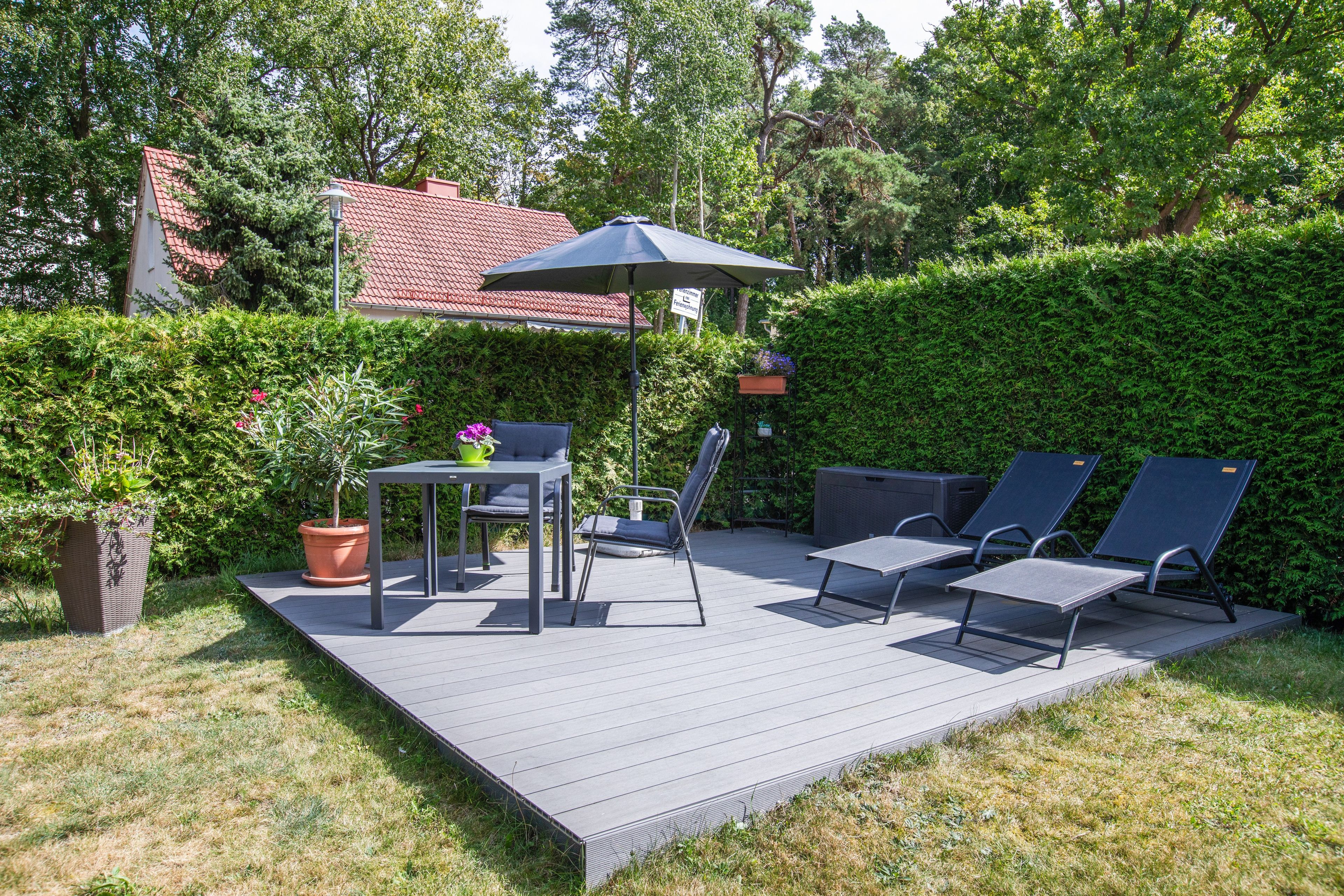 Een terras buiten met een tafel, stoelen, een bloempot en een grote parasol.