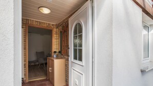 A doorway leading to a room with a tiled floor, a wooden cabinet, and a window with a decorative frame. - Apartment “Max” with Private Terrace, Garden, and Wi-Fi (Heringsdorf)