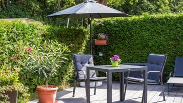 Eine Terrasse im Freien mit Tisch und Stühlen, umgeben von Pflanzen und einer Hecke.