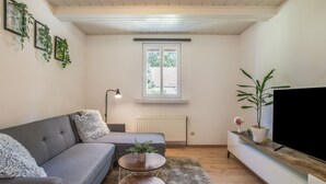 A modern living room with a grey sofa, two round wooden side tables, a fluffy grey rug, a large window with a view, a radiator, and a TV on a wooden stand. - Apartment “Max” with Private Terrace, Garden, and Wi-Fi (Heringsdorf)