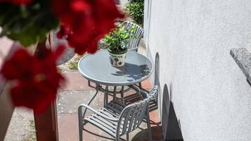Ein Sitzbereich im Freien mit einem runden Tisch, zwei Stühlen, einem Blumentopf und einem an der Wand montierten Stromkasten.