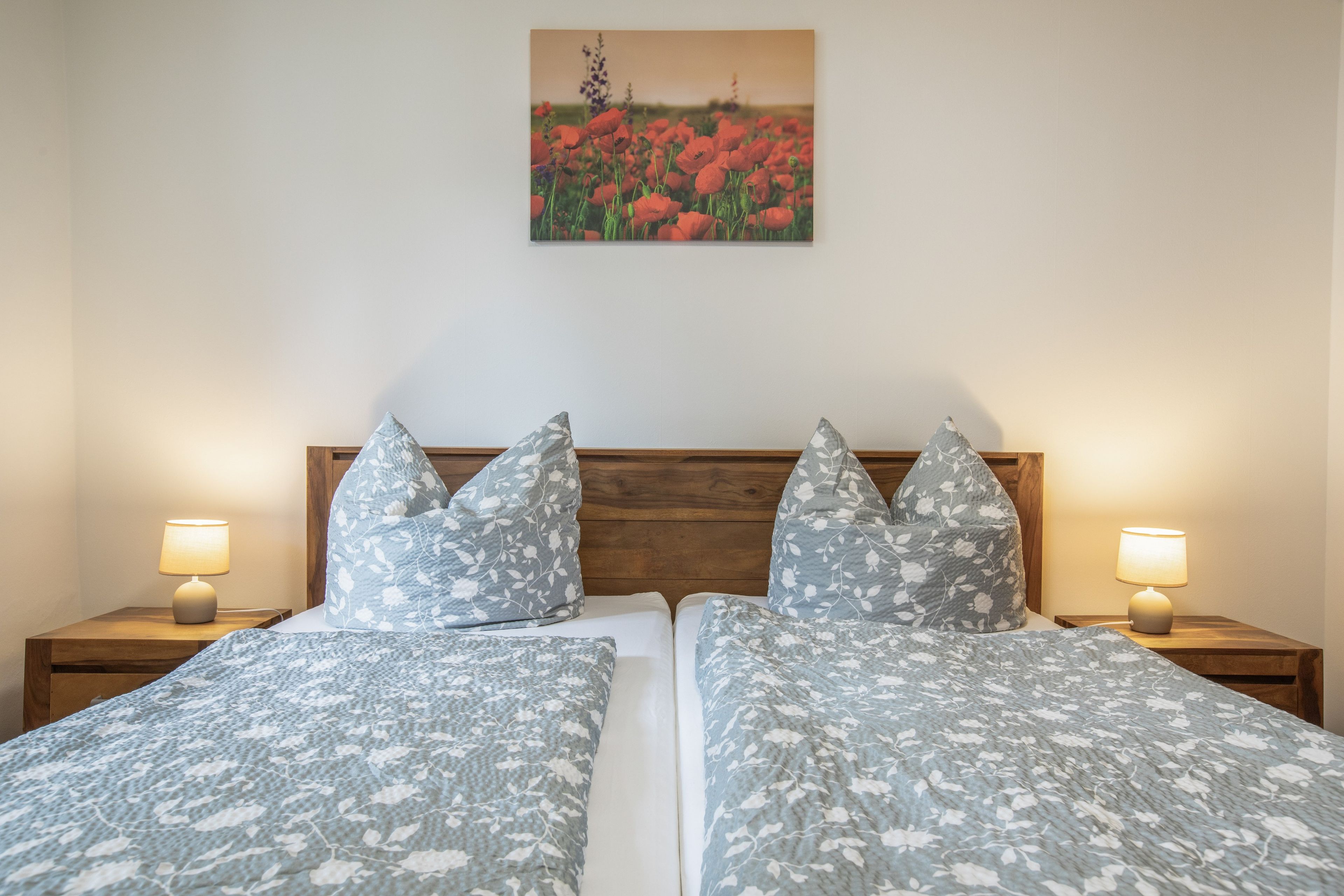 Ein Doppelbett mit floraler Bettwäsche, zwei Nachttischlampen und ein Gemälde mit Mohnblumen an der Wand.