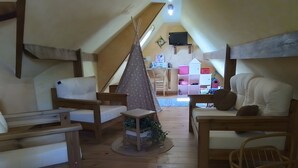 Tunnelmallinen ullakkohuone, jossa on puuhuonekaluja, teepeeteltan näköinen leikkitila ja seinälle asennettu televisio.