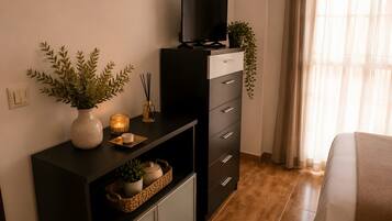 A modern room with a TV on a black cabinet, a potted plant, a candle, and a small table with a basket and a vase.