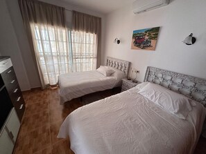 Une chambre avec deux lits, une fenêtre avec des rideaux, un tableau au mur et une commode.