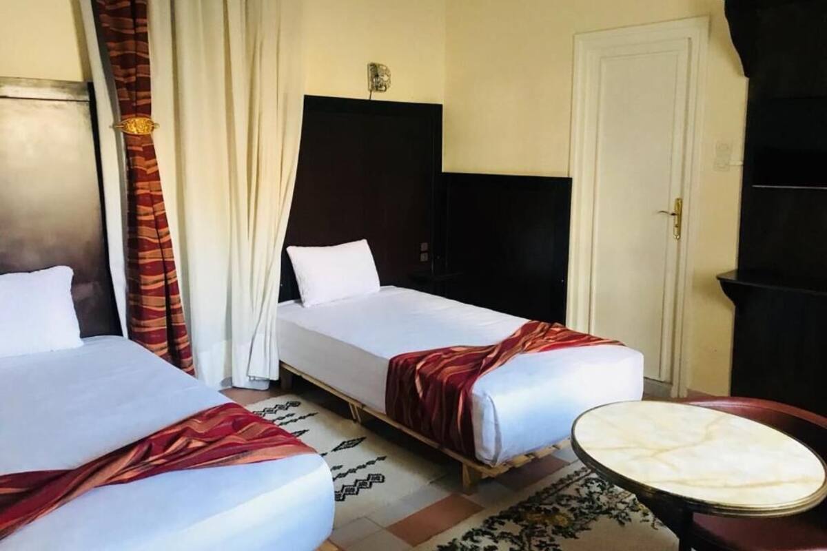 Habitación de hotel con dos camas, una mesita redonda pequeña, un televisor y una puerta.