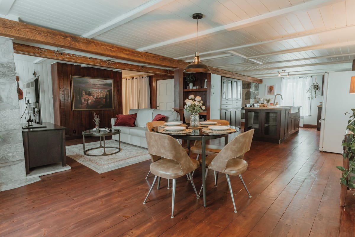 Een ruime woonkamer met een eettafel, stoelen en een bank. Er is een keuken met kastjes en een spoelbak.