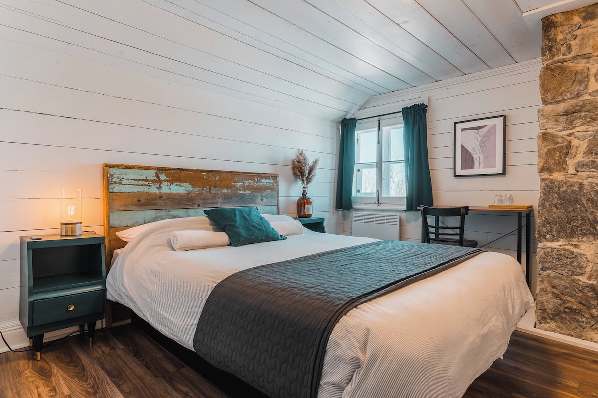 Een slaapkamer met een bed, nachtkastje, tafel en een stenen muur.