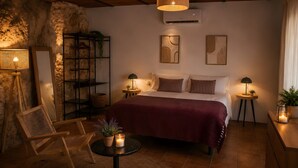 Une chambre à coucher comprenant un lit, deux tables de chevet, une chaise, une petite table avec des bougies et des œuvres d’art murales.