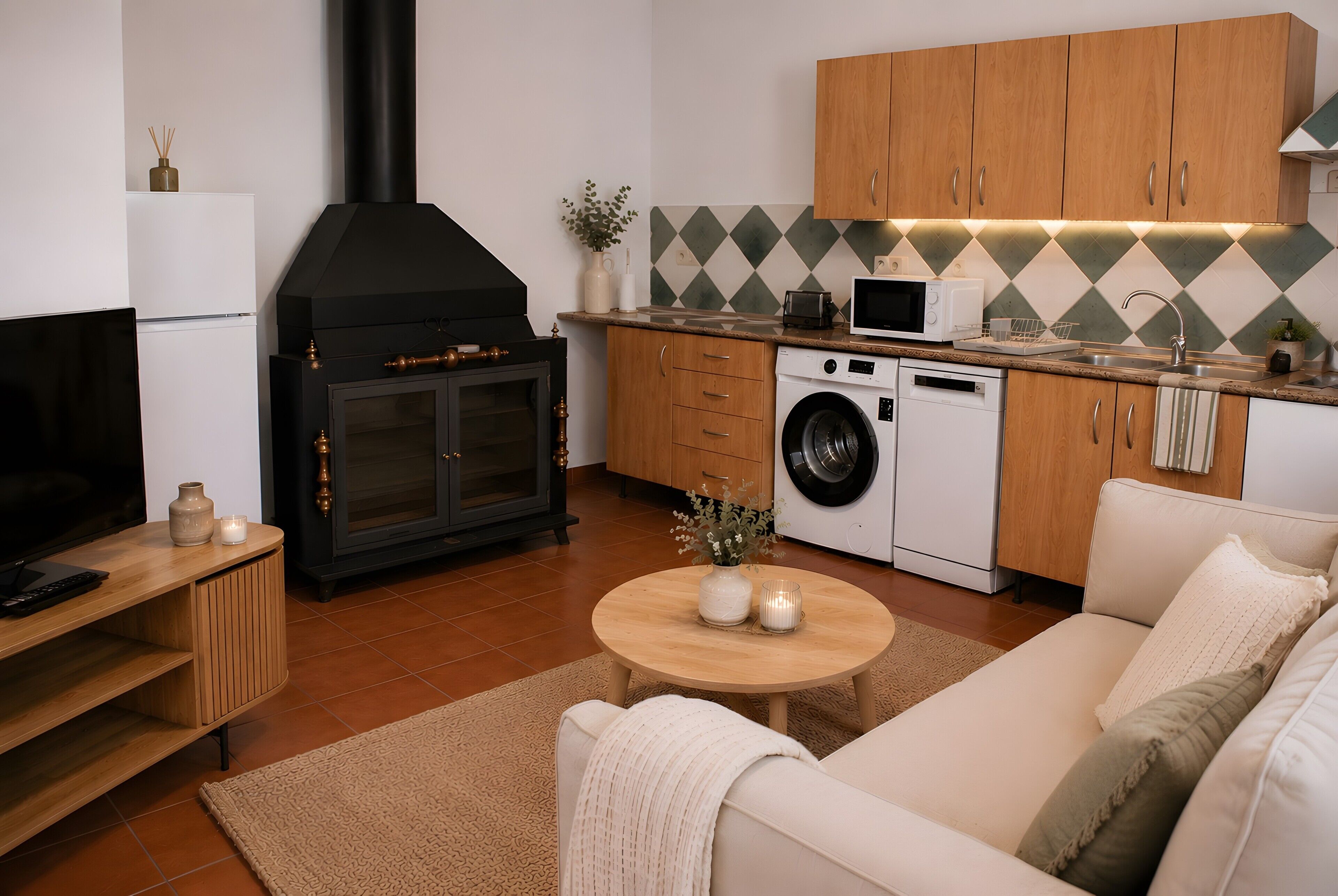Una cocina moderna con horno empotrado, microondas y lavadora, un sofá y un televisor.