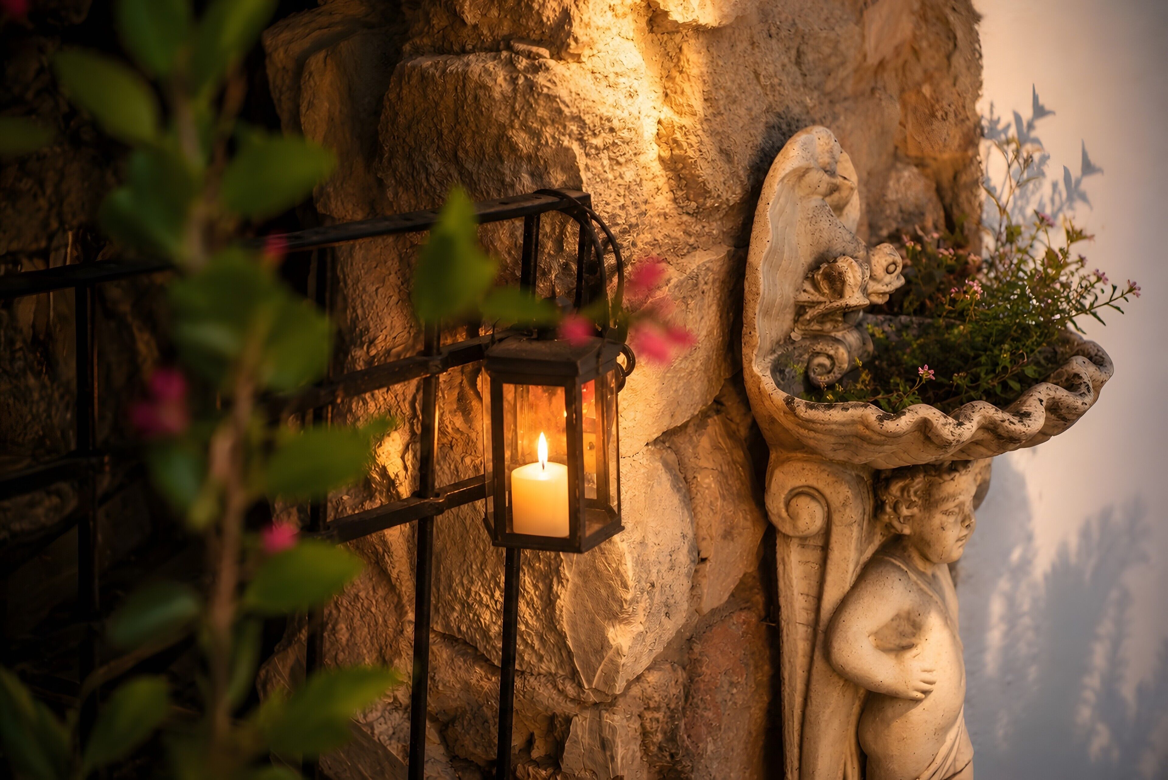 A stone wall with a candle in a lantern, a decorative angel, and a plant pot.