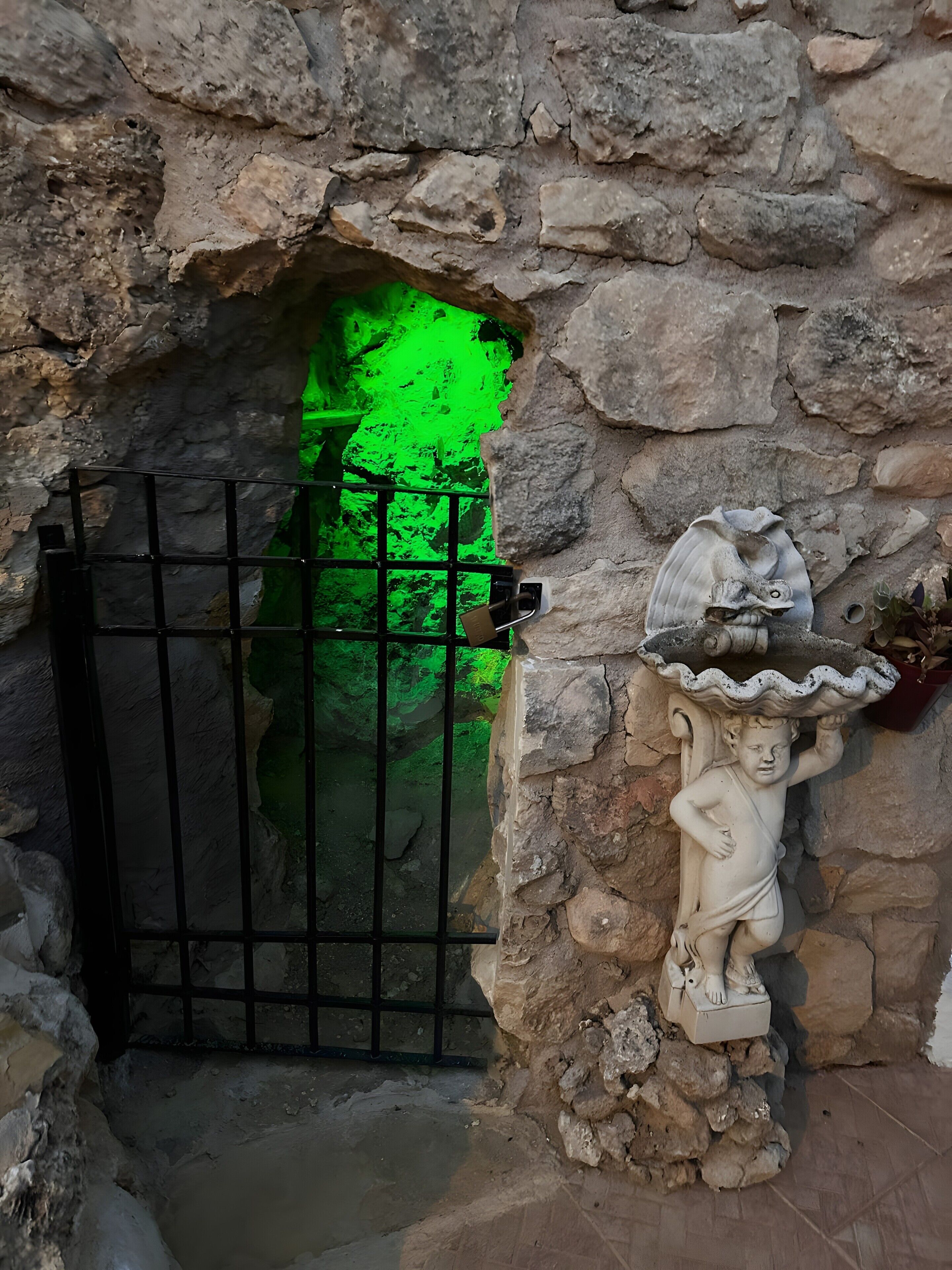 Un muro de piedra con una reja de metal y una figura decorativa.
