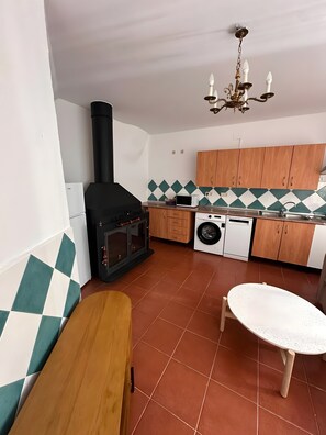 Uma cozinha compacta com fogão a lenha, máquina de lavar e um espaço de refeições com banco.
