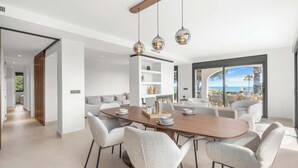 A modern dining area with a wooden table and six chairs, a white shelving unit, and a view of the ocean. - Stunning villa Dolce vita - ref 69 (Las Lagunas de Mijas)