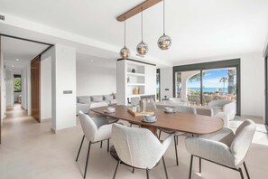 A modern dining area with a wooden table and six chairs, a white shelving unit, and a view of the ocean. - Stunning villa Dolce vita - ref 69 (Las Lagunas de Mijas)