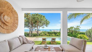 A modern living room with a sofa, a coffee table, and a view of a pool and garden. - Stunning villa Dolce vita - ref 69 (Las Lagunas de Mijas)
