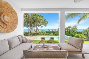 A modern living room with a sofa, a coffee table, and a view of a pool and garden. - Stunning villa Dolce vita - ref 69 (Las Lagunas de Mijas)
