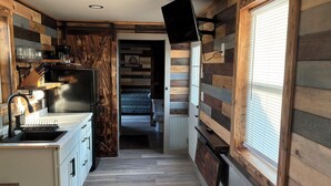 A kitchen with a built-in TV, wooden walls, and a view into the living area. - Cozy 1-bedroom cabin in Protection with cool AC (Protection)