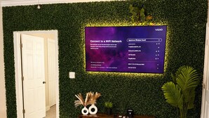 Uma sala de estar moderna com uma parede verde, uma TV de tela plana, uma mesa de centro de vidro, um sofá e um armário de madeira.