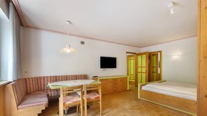 A room with a bench, a table, a bed, and a TV. - Apartment '8 Residence Ciasa Ulli Typ B' with Mountain View, Shared Terrace and Wi-Fi (San Cassiano)