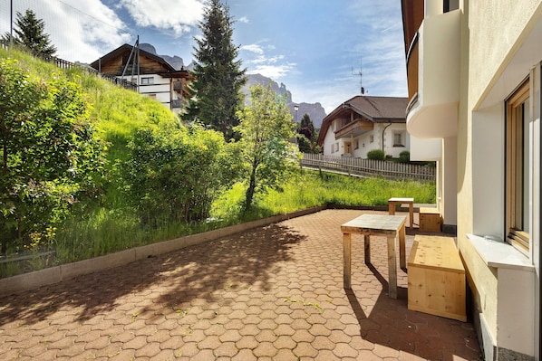 Une terrasse dallée avec des carreaux hexagonaux, des bancs en bois et une vue sur une colline parsemée de bâtiments et d’arbres.
