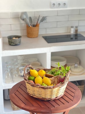 Ein Korbkörbchen mit Zitronen und Kräutern auf einem runden Holztisch in einer Küche mit weißen Schränken und einer gefliesten Spritzschutzwand.