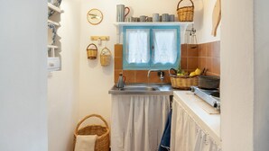 Uma cozinha compacta com janela, prateleiras com louças, pia e fogão.
