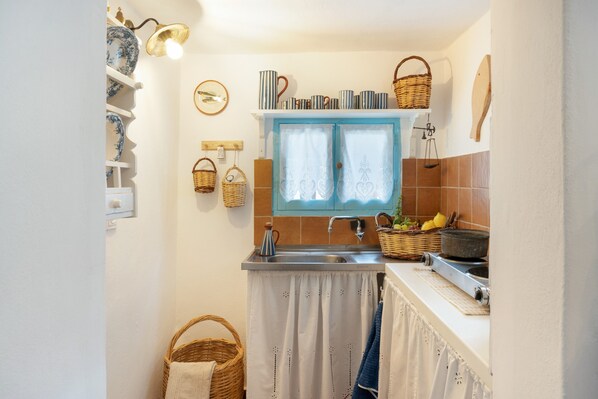 A compact kitchen with a window, shelves with dishes, a sink, and a stove.