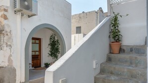 Uma rua estreita com um edifício branco, uma porta de madeira, um vaso de planta e uma escadaria de pedra.