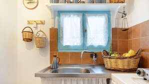 Uma cozinha com pia, janela com cortinas, cesta de frutas e uma balança pendurada.