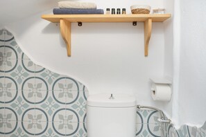 A bathroom with a toilet, a shelf with toiletries, and patterned tiles.