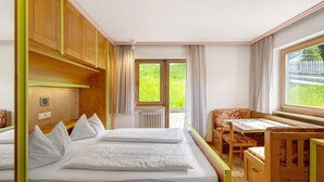 A room with a bed, a small table, a chair, and a window with a view of greenery. - Apartment '7 Residence Ciasa Ulli Typ A' with Mountain View, Shared Terrace and Wi-Fi (San Cassiano)
