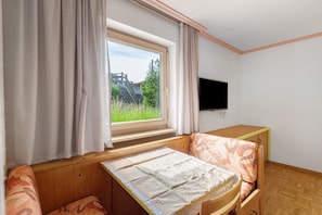 Una stanza con un letto, una TV, una finestra con tende e vista sul verde circostante.