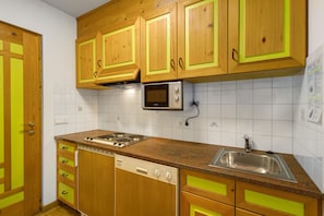 Cucina con pensili e basi in legno, forno a microonde, lavastoviglie e lavello.