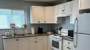 A modern kitchen with white cabinetry, a stainless steel sink, a built-in oven, and a refrigerator. - Family Friendly Suite (Langley Township)