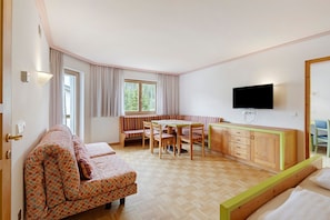 Una habitación compacta con sofá, una mesa de comedor con sillas, una kitchenette y un televisor en la pared.