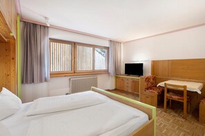 Ein Hotelzimmer mit Bett, Schreibtisch, Stuhl, Fernseher und einem Fenster mit Jalousien.