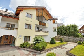 A multi-story building with balconies, a sign reading 'Ciesa UBT,' and a well-maintained garden area. - Apartment '3 Residence Ciasa Ulli Typ A' with Mountain View, Shared Terrace and Wi-Fi (San Cassiano)
