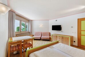 Ein Schlafzimmer mit einem Bett, einem Schreibtisch, zwei Stühlen, einem Fernseher und einem Fenster.