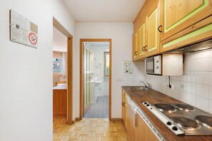 A kitchen with wooden cabinets, a microwave, a stove, and a sink. - Apartment 'Residence Ciasa Ulli Typ B' with Wi-Fi (San Cassiano)