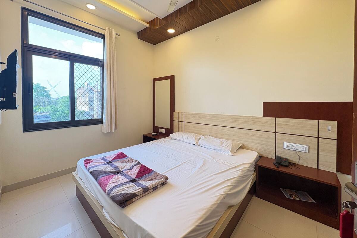 Une chambre d’hôtel comprenant un lit, une table de chevet, un miroir, une fenêtre avec des rideaux et un ventilateur de plafond.