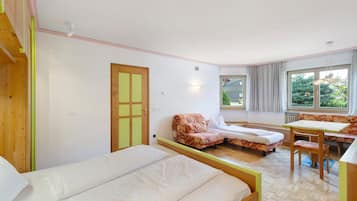 A room with two beds, a sofa, a table, and a window with a view.
