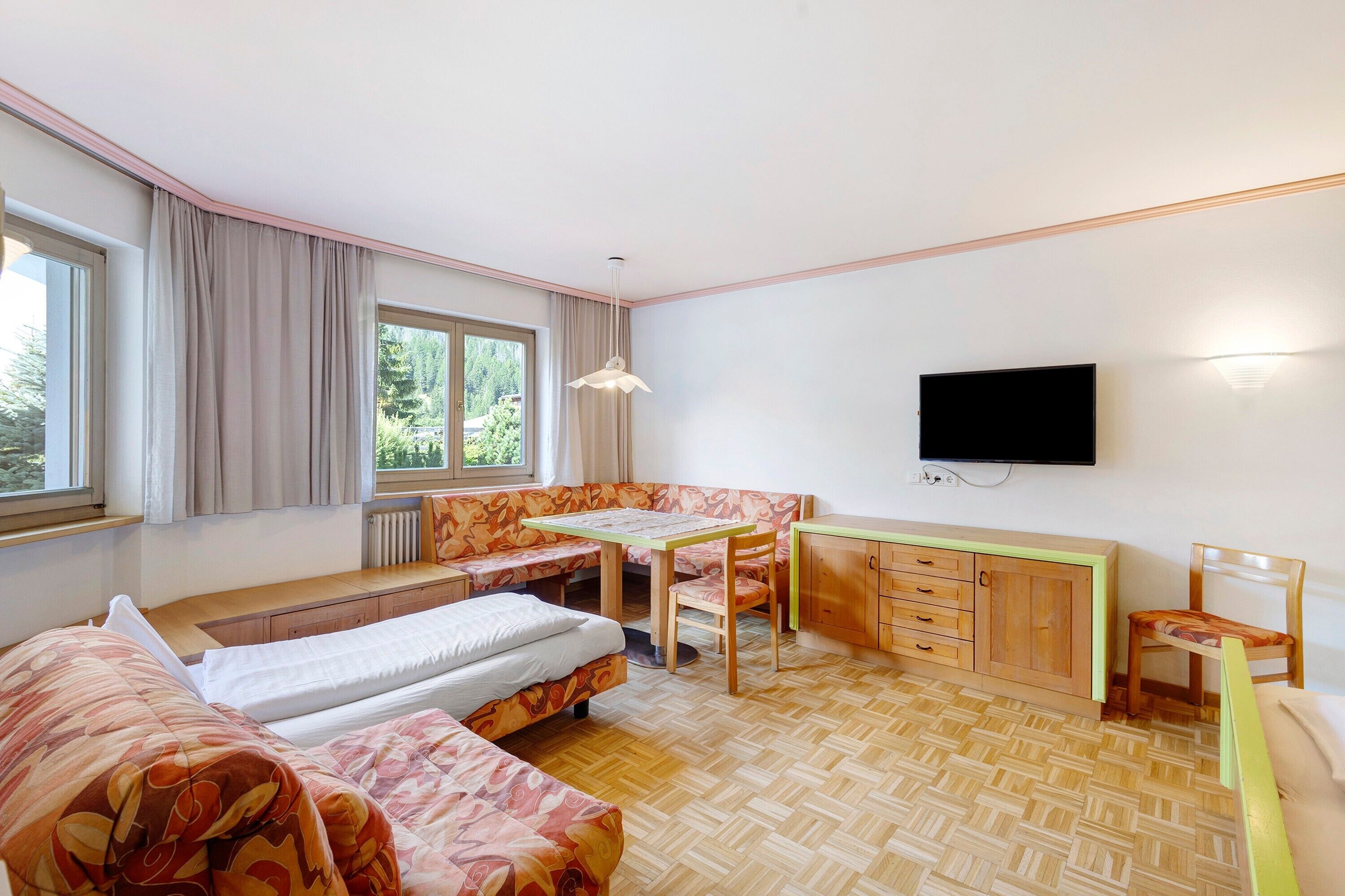 A room with two beds, a dining table, a TV, and a window with curtains.