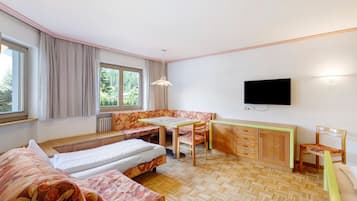 A room with two beds, a dining table, a TV, and a window with curtains.
